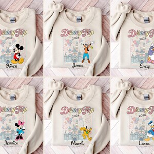 May include: Cream-coloured sweatshirts with Disney character graphics. Each sweatshirt features a different character, the text "Disney Trip 2020", and a name. Characters include Mickey Mouse, Goofy, Daisy Duck, Minnie Mouse, Pluto, and Donald Duck.