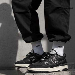 May include: Black and white trainers with the number "882" on the side. The trainers have a white sole and black laces. The image also shows black trousers and white socks with the word "LESS." printed on them.