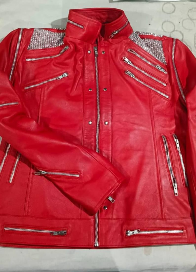 May include: A vibrant red leather jacket featuring a stand-up collar, multiple silver-toned metal zips across the chest and sleeves, and decorative silver rhinestone panels on both shoulders. The front includes a central zip closure.