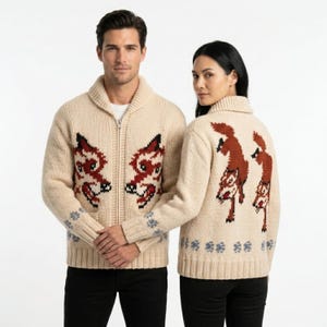 May include: A cream-colored knit zip-up cardigan featuring a shawl collar and a repeating fox motif in shades of brown, black, and white. The design includes a row of small blue floral patterns near the ribbed hem and cuffs, with a full-length zipper.