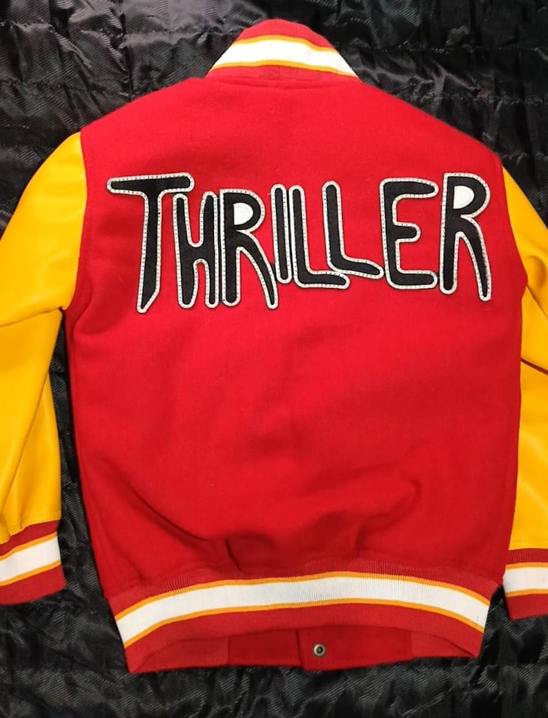 May include: A red varsity jacket with yellow sleeves and a white and yellow striped collar, cuffs, and hem. The back features the word THRILLER in large, black, white-outlined letters. The jacket has a snap-button front closure and a red body.