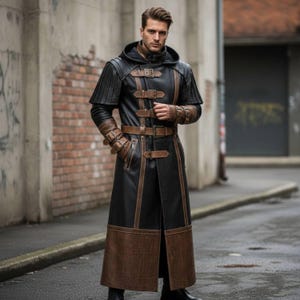 Può includere: Un lungo cappotto in pelle nera con dettagli marroni, caratterizzato da un design con cappuccio e molteplici chiusure con fibbia. Il cappotto ha una vestibilità sartoriale ed è adatto all'abbigliamento.