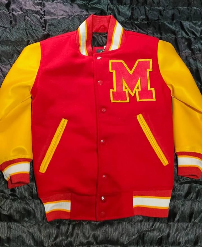 May include: A red varsity jacket with yellow sleeves, featuring a large red letter M with a yellow border on the left chest. The jacket has a snap-button front closure, two yellow-trimmed pockets, and striped ribbed cuffs and hem in red and white.