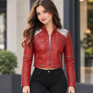 May include: A red jacket featuring silver sequin shoulder panels, multiple diagonal silver-toned zippered pockets on the chest, and a central front zipper closure. The jacket has long sleeves with additional zippered details and a cropped hemline.