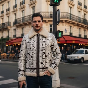 Puede incluir: Chaqueta con estampado de piel de serpiente en blanco y marrón, con cuello y puños de borrego crema. La chaqueta tiene cierre de cremallera y ribetes marrones. La persona está en una calle de la ciudad.