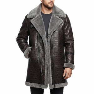 Könnte beinhalten: Ein brauner Ledermantel mit Krokodilmuster. Der Mantel hat einen grauen Shearling-Kragen und -Futter mit Shearling-Besatz an den Manschetten und am Saum. Der Mantel hat einen Reißverschluss und einen Knopf. Der Mantel ist ca. 122 cm lang.