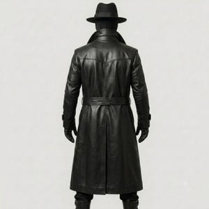 Op de afbeelding: Een zwarte leren trenchcoat met een ceintuur in de taille, lange mouwen en een gestructureerde kraag. Het ensemble bevat een bijpassende zwarte fedora-hoed en zwarte leren handschoenen, wat een monochroom uiterlijk geeft vanaf de achterkant.