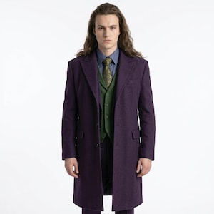 May include: A long, purple overcoat with a notched lapel. The coat is worn over a green vest, a patterned tie, and a blue shirt. The outfit is completed with dark pants. The person has long brown hair.