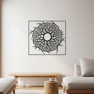 May include: Black and white wall art featuring a circular tree design. The artwork is framed in a square black frame and mounted on a white wall. The tree design has intricate branches and a central open circle.