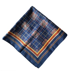 May include: A navy blue silk scarf with a plaid pattern in white, orange, and brown. The scarf is square-shaped and has a contrasting border in orange and brown. The fabric has a slight sheen.
