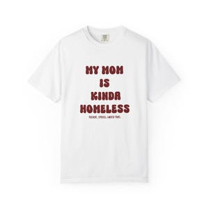 Op de afbeelding: Een wit T-shirt met korte mouwen en donkerrode tekst die in een vet, afgerond lettertype MY MOM IS KINDA HOMELESS luidt, met de kleinere tekst PLEASE, SPEED, I NEED THIS. direct daaronder gedrukt in dezelfde donkerrode kleur.