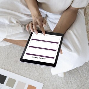 Op de afbeelding: Een zwarte tablet met een werkblad getiteld "Limiting Beliefs" met paarse accenten. De tablet wordt vastgehouden door een persoon die witte kleding draagt. Een kleurenpalet is zichtbaar in de linker benedenhoek.