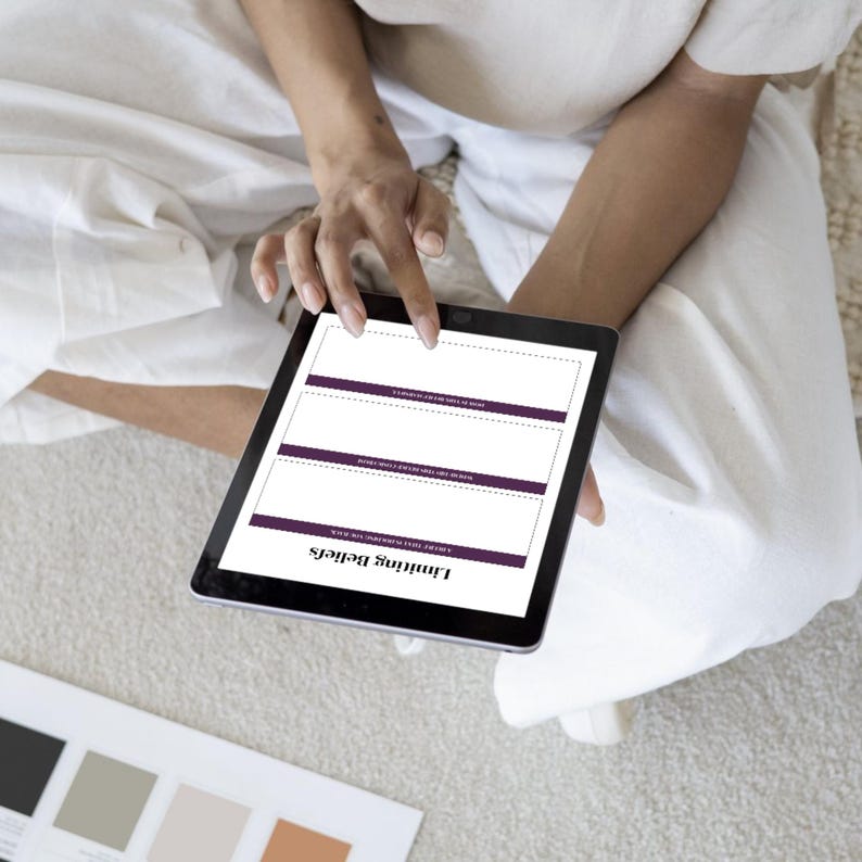 Op de afbeelding: Een zwarte tablet met een werkblad getiteld "Limiting Beliefs" met paarse accenten. De tablet wordt vastgehouden door een persoon die witte kleding draagt. Een kleurenpalet is zichtbaar in de linker benedenhoek.