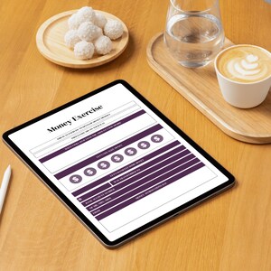 Op de afbeelding: Een digitale tablet met een "Money Exercise" werkblad, met secties voor budget, doelen en details van geldoverdrachten. De afbeelding bevat een kopje koffie, een glas water en een bord met kokossnoepjes op een houten oppervlak.
