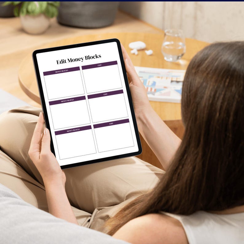 Op de afbeelding: Een zwarte tablet met een sjabloon voor financi&euml;le planning met de titel "Edit Money Blocks". De sjabloon bevat zes rechthoekige blokken met koppen in een donkerpaarse kleur. De tablet wordt door een persoon vastgehouden.