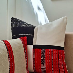 May include: Three decorative throw pillows with patterned fabric. One pillow is black and white, another is beige with red stripes, and the third is white, black, and red. The pillows are on a beige couch.