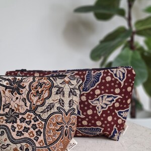 May include: Two patterned cosmetic bags. One bag features a floral design in shades of brown, beige, and black. The other bag has a maroon background with a blue and white floral pattern. Both bags have a zip closure.