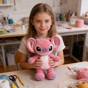 Puede incluir: Una muñeca rosa de ganchillo hecha a mano con orejas grandes, ojos negros y nariz morada. La muñeca está sujeta por una persona. Los brazos y las piernas de la muñeca también son rosas, con detalles morados en los pies. Es un artículo hecho a mano.