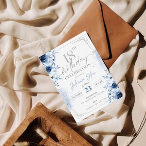 May include: An invitation for an 18th birthday celebration. The invitation features a floral design in shades of blue and gray, with the text "18th Birthday Celebration" and the honoree's name, date, and time. The invitation is accompanied by a brown envelope.