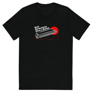 May include: Black t-shirt with a white and red graphic. The graphic features a harmonica with the text "Real Harmonicas Have a Button" in white. A red circle is behind the harmonica.