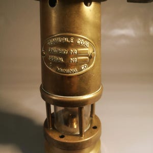 May include: Vintage brass miner's lamp with a handle and a glass enclosure. The lamp features an oval plaque with the text "FERNDALE COAL COLLIERY NO. 2 SERIAL NO. 9 MINING CO." The lamp is a cylindrical shape with a circular base.