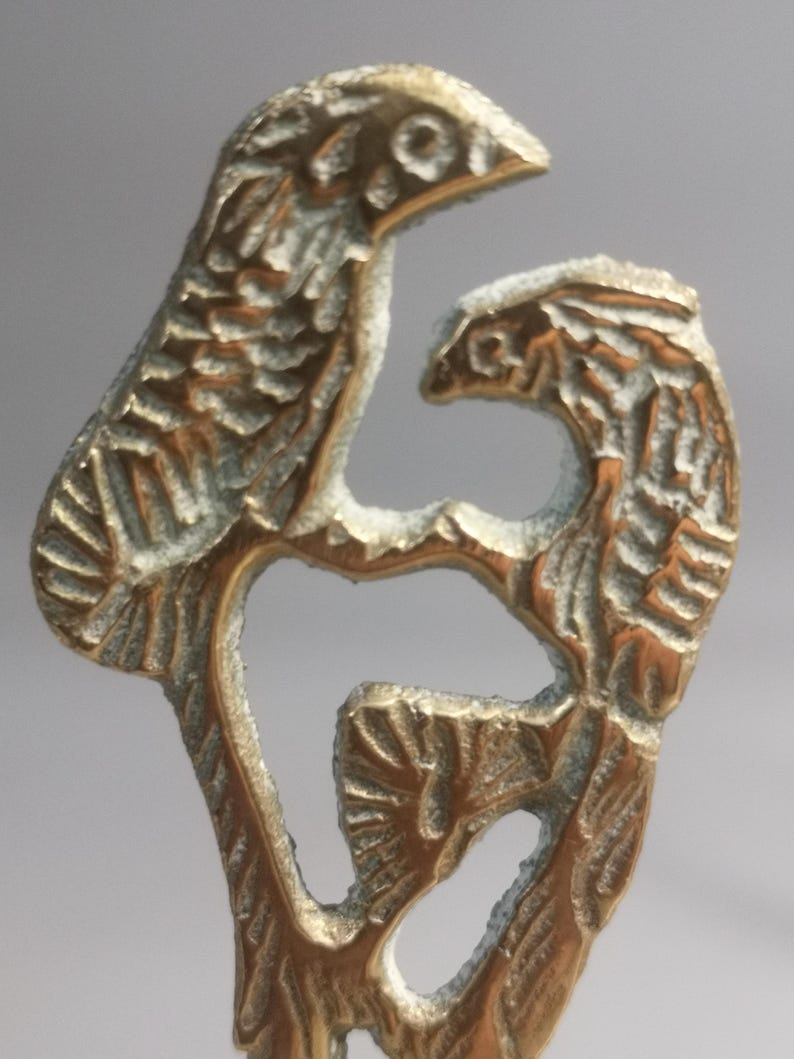 May include: A detailed brass sculpture featuring two birds perched on a branch. The birds have textured feathers and are facing each other. The sculpture has a vintage look with a slightly tarnished finish.