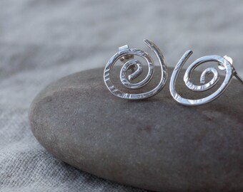 May include: A pair of silver spiral stud earrings. The earrings are made of textured metal and have a simple, modern design.