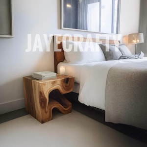 Puede incluir: Una mesita de noche de madera natural con un diseño orgánico único. La mesa está junto a una cama con ropa de cama blanca y una manta gris. Una vela y libros están encima de la mesa. El texto "JAYECRAFTY" está en la parte superior de la imagen.