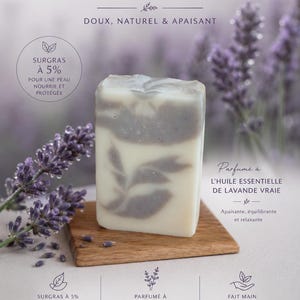 Puede incluir: Una pastilla de jabón natural con aceite esencial de lavanda, sobre una pequeña tabla de madera. El jabón es blanco con remolinos de lavanda y el texto "SAVON NATUREL". Ramas de lavanda en el fondo. El jabón es suave, natural y calmante.