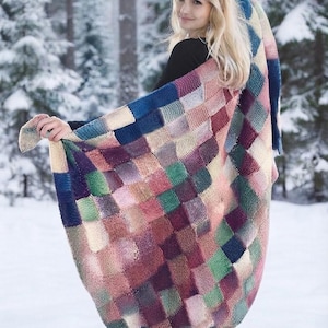 May include: A large, rectangular knitted blanket featuring a multi-coloured patchwork design composed of small, individual squares in shades of deep blue, forest green, soft pink, cream, burgundy, and muted purple, creating a textured, grid-like pattern.