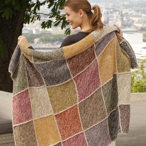 Può includere: Una coperta rettangolare in maglia con un design patchwork di quadrati multicolori nelle tonalità giallo senape, rosso scuro, verde oliva, blu navy e crema. Ogni quadrato è unito da un bordo in filo color crema lavorato a punto legaccio.