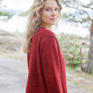 May include: A deep red long-sleeved knit sweater featuring a subtle textured pattern throughout the fabric. The garment has a round neckline and a straight hemline, constructed from a soft, fuzzy yarn material with visible knit stitches.
