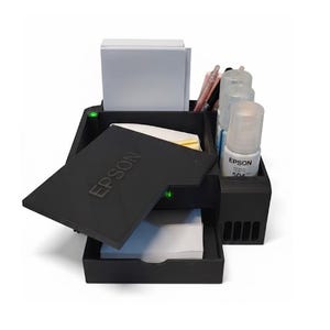 May include: A black Epson printer ink station with multiple compartments. The station holds white paper, ink bottles, and pens. The Epson logo is visible on the lid. The station is designed to organize printer supplies.