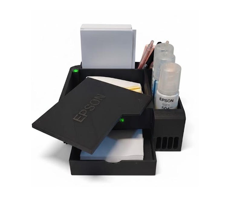 May include: A black Epson printer ink station with multiple compartments. The station holds white paper, ink bottles, and pens. The Epson logo is visible on the lid. The station is designed to organize printer supplies.