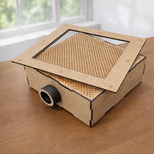 Könnte beinhalten: Eine rechteckige, hellbraune Holzkiste mit perforierter Oberseite und abnehmbarem Rahmen. Der Rahmen ist mit kleinen messingfarbenen Befestigungselementen befestigt. Eine kreisförmige, schwarz-braune Komponente ragt aus der Seite der Kiste heraus.