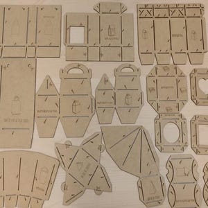 May include: A collection of laser-cut, unfinished wooden packaging templates. Various shapes include boxes with handles, gift tags, and decorative cutouts. Each piece features etched lines for folding and assembly, with a shopping bag icon.