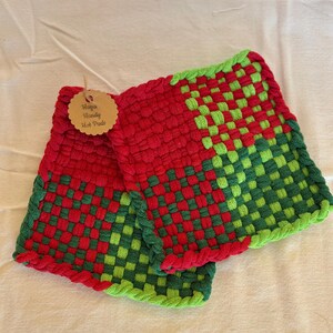 Könnte beinhalten: Zwei handgefertigte, rot-grün gewebte Topflappen. Die Topflappen haben ein Schachbrettmuster aus roten und grünen Quadraten. Auf dem Etikett steht "Haya's Handy Hot Pads".