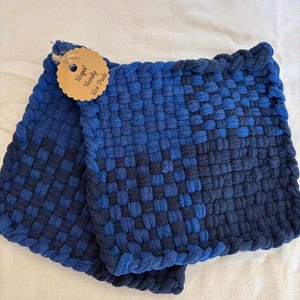 May include: Two blue woven hot pads. The pads are made of a dark and light blue woven material. A small, round tag with the words "Hayes' Handy Hot Pads" is attached to one of the pads.