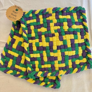 Puede incluir: Salvamanteles tejidos en amarillo, verde y morado. Las almohadillas tienen un borde verde trenzado y una etiqueta que dice "Hayes' Handy Hot Pads". Las almohadillas están hechas de un material tejido.