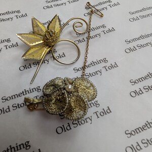 May include: A vintage gold-toned brooch and pin set. The brooch is a cluster of textured flowers with a pearl center. The pin features a floral design and a chain connecting to a decorative element. The background has the text "Something Old Story Told".