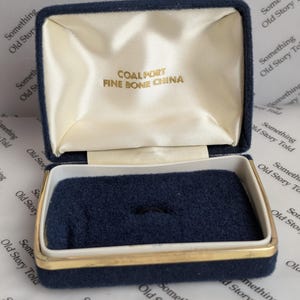 May include: A vintage blue velvet jewellery box with a gold trim. The interior has a cream satin lining and a dark blue velvet base with a ring holder. The text "COALPORT FINE BONE CHINA" is printed inside the lid.
