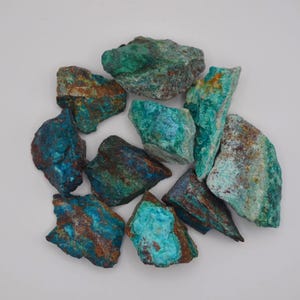 Peut inclure: Une collection de pierres minérales de chrysocolle brutes et non polies présentant un mélange vibrant de teintes turquoise, bleu sarcelle et bleu profond avec des stries contrastées de matrice brun terreux et rouille sur les surfaces rocheuses.