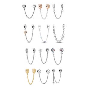 Può includere: Una collezione di catene di sicurezza per charm in argento e oro. I charm presentano vari design, tra cui cuori, stelle e motivi floreali. Le catene sono progettate per essere attaccate ai braccialetti.