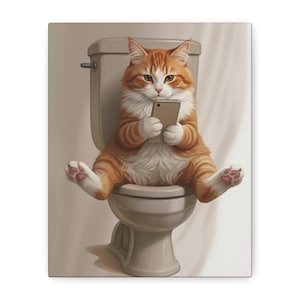 May include: A canvas print featuring a ginger and white cat sitting on a toilet, engrossed in a smartphone. The cat's paws are visible, and the toilet is a neutral gray color. The background is a soft, off-white.
