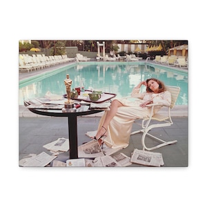 May include: A vintage photograph depicts a woman relaxing by a pool. She is seated in a chair, wearing a cream-colored outfit and black heels. A table holds an Oscar statue, drinks, and a tray. Newspapers are scattered on the ground.