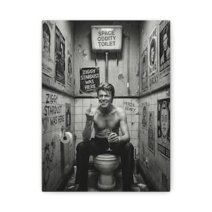 Puede incluir: Impresión en lienzo en blanco y negro que muestra a un hombre sentado en un inodoro, sosteniendo un vaso y un cigarrillo, con el dedo medio levantado. Las paredes están cubiertas de carteles y grafitis, incluyendo los textos "ZIGGY STARDUST WAS HERE" y "SPACE ODDITY TOILET."