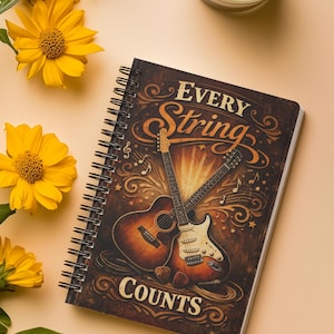 May include: A spiral-bound notebook with a dark brown cover featuring an illustration of an acoustic and an electric guitar crossed over each other. The text "EVERY String COUNTS" is printed in a decorative font, surrounded by musical notes.