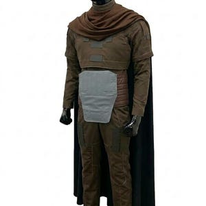 May include: A brown long-sleeved costume set featuring a dark brown cowl, a chest plate, a light grey abdominal armour piece, and a long black cape. The outfit includes matching brown trousers with reinforced panels and is displayed on a black mannequin.