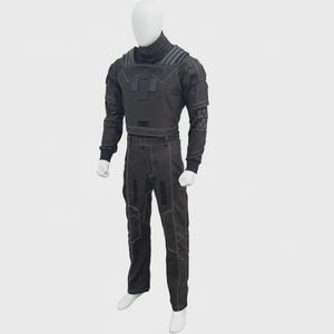 May include: A dark gray tactical-style two-piece outfit consisting of a long-sleeved top with a high collar, ribbed shoulder detailing, and a matching pair of trousers. The set features prominent white contrast stitching, rectangular patches, and geometric patterns on the sleeves.