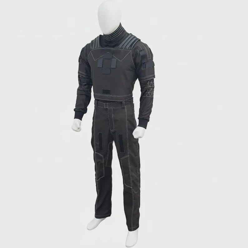 May include: A dark gray tactical-style two-piece outfit consisting of a long-sleeved top with a high collar, ribbed shoulder detailing, and a matching pair of trousers. The set features prominent white contrast stitching, rectangular patches, and geometric patterns on the sleeves.